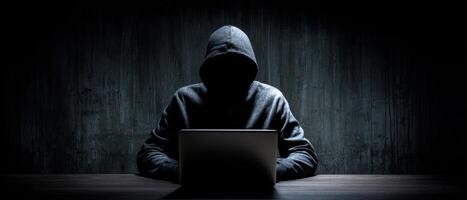 The mysterious hacker working intently on a laptop in a dimly lit environment. photo