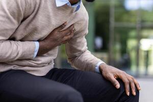 An African American man experiencing chest pain, possibly a heart attack, captured in a close-up shot. Focus on the hands and upper body. photo