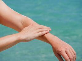 A man on the beach applies sunscreen lotion to his hands at the background of sea water. Skincare, sun protection and beach holidays concept photo