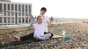 Mother and her young daughter exercising together on rooftop, bonding through fitness activities with dumbbells, promoting healthy family lifestyle and active habits for well-being and positive energy video