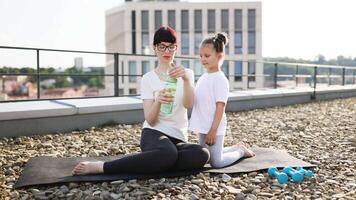 Mother and young daughter spending time outdoors on rooftop, practicing fitness and hydration. Bonding moment focusing on healthy habits and mutual encouragement. video