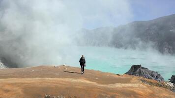 Aerial view of woman walking towards the edge of Ijen Volcano crater lake in East Java, Indonesia. Turquoise water, sulfur steam, and surreal volcanic landscape. Concept of nature, travel, adventure. video