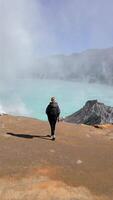 Aerial view of woman walking towards the edge of Ijen Volcano crater lake in East Java, Indonesia. Turquoise water, sulfur steam, and surreal volcanic landscape. Concept of nature, travel, adventure. video