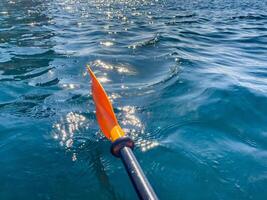 Paddle Water Kayaking - Close-up of a red and black paddle moving through turquoise water on a sunny day. photo