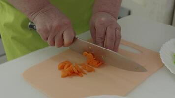 Professional chef's hands precisely slicing bright orange carrots on wooden cutting board, showcasing expert culinary knife skills during ingredient preparation for fresh vegetable dish video