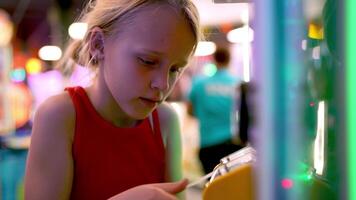Blonde girl in red top inserting arcade tickets into yellow counting machine in game center video