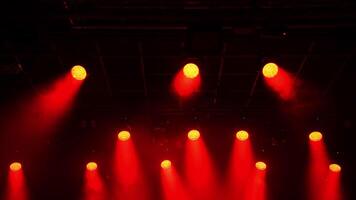 Metal grid hosting powerful red spotlights creating dramatic illumination, casting intense beams across dark concert hall staging area before upcoming performance video