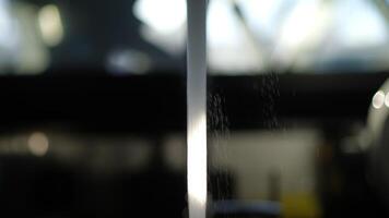 Stream of running tap water captured in strong backlight with visible droplets and kitchen background video