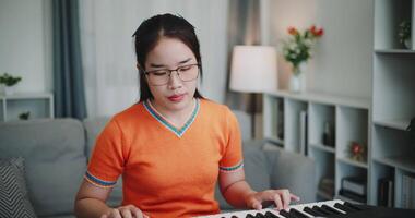 Handheld medium shot, Asian woman is relaxing and enjoying playing music on an electronic keyboard in a quiet house. Leisure activities at home video