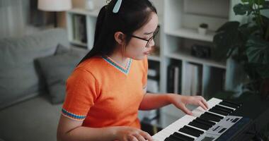 Handheld high angle view shot, Asian woman is relaxing and enjoying playing music on an electronic keyboard in a quiet house. Leisure activities at home video