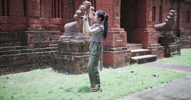 Handheld shot, Happy young woman is enjoying a quiet stroll, taking photos of old sculptures and ancient brick structures, Enjoy holiday travel. video