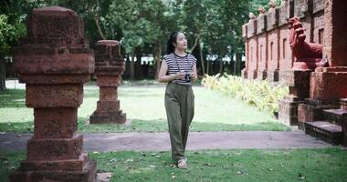 Handheld shot, Happy Asian woman is enjoying a quiet stroll, taking photos of old sculptures and ancient brick structures, Enjoy travel. video