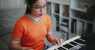 Handheld high angle view shot, A young Asian woman is happily playing a keyboard in a cozy living room. Enjoy favorite musical instruments video