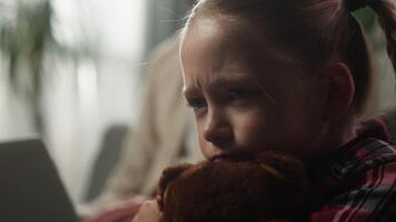 Sad upset little Caucasian daughter lonely girl hugging teddy bear at home near busy father working on laptop ignoring child family conflict emotional stress distant relationship indoor bad childcare video