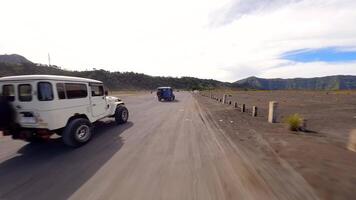 Cinematic FPV drone shot of jeeps driving across volcanic black sand plains near Mount Bromo in East Java, Indonesia. Concept of travel, tour, and adventure. video