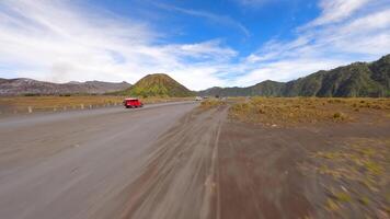 Cinematic FPV drone shot of jeeps driving across volcanic black sand plains near Mount Bromo, with lush mountain backdrop in East Java, Indonesia. Concept of travel, tour, and adventure. video