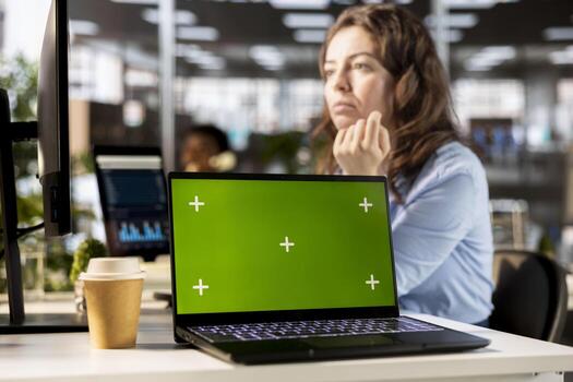 Focused administrator solving tasks at the office next to copy space display, using data analytics and financial reports. Professional woman looks at the current situation, multitasking. photo