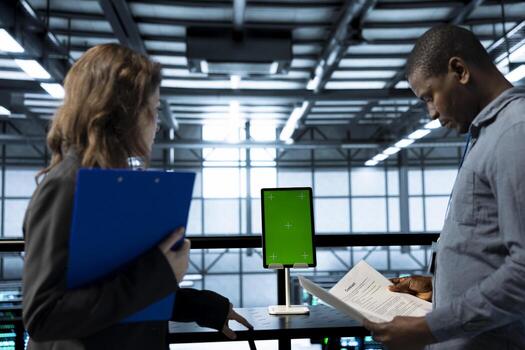 Inspector checking documents in server hub to ensure compliance with industry standards and using greens screen tablet. Admin inspecting files, overseeing data center workplace security protocols photo