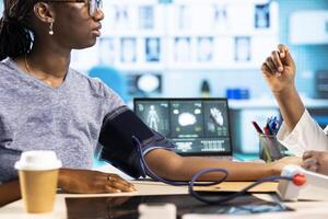 Woman medic expert measuring blood pressure at a consultation with patient, using blood pressure monitor gadget in the medical office. Cardiology measurement readings at checkup. photo