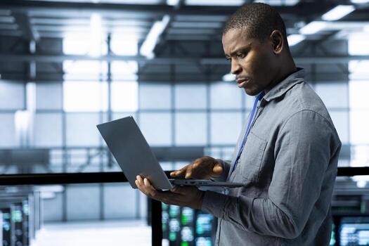 Engineer in data center operating laptop, deploying new server architectures, configuring network virtualization, verifying settings, updating storage arrays, maintaining stable network performance photo