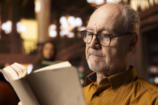 Elderly retired person with spectacles having a reading hobby at the public library, enjoying lecture for leisure activity during retirement. Wrinkled happy man with wisdom and skill, literature. photo