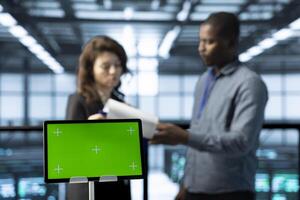 Mockup laptop in front of data center engineers in blurry background calibrating energy usage. Close up of isolated screen notebook used by server hub workers inspecting UPS configurations photo