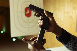 Close up of hands loading handgun magazine at indoor shooting range with paper target in blurry background. Person doing firearm training, learning how to responsibly reload pistol photo