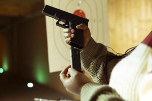 Close up of person reloading magazine into pistol during firearm practice session at indoor shooting range, learning safety practices. Shooting range client loading gun, doing self defense preparation photo