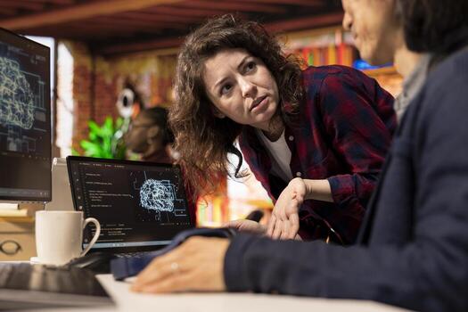 Programmer coming to AI startup office CTO manager desk to request help with building application. Employee asks questions to senior team leader in artificial intelligence software development agency photo