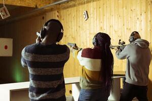 Friends having fun in shooting gallery using guns to hit targets with ammo. Mates entertained by shooting bullseyes at indoor firing range facility, competing against each other photo