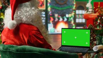 Santa Claus making list of kids who has been naughty or nice on green screen laptop. Person preparing travel plans on chroma key notebook before visiting children, camera A photo