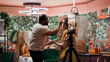 Artists recording creative process of painting an artwork piece, hosting online art class for instruction and remote learning. Diverse painters showing supplies and paint tubes used. Camera b. photo