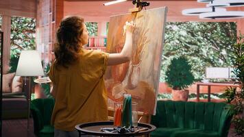 In a rustic workshop, artist mixes a variety of watercolor paint on palette to create a colorful masterpiece on canvas. Woman painting with a brush and showing her skill, artwork creation. Camera B. photo