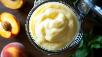 Fresh Peach Smoothie in Blender Jar with Ripe Peaches and Leaves photo
