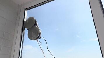 Robot vacuum cleaner washes windows with two gray microfiber attachments on a sunny day video