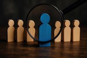 Magnifying glass highlighting a unique blue wooden figure, symbolizing selection and individuality photo