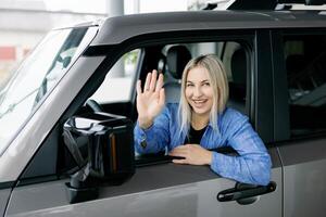 Happy customer waving from new car window at dealership photo