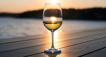 A glass of wine on a wooden table with the sun setting in the background photo