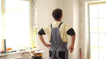 Construction worker in overalls crossing arms while planning a renovation project in an empty room, with tools neatly arranged on the windowsill, ready for upcoming tasks video