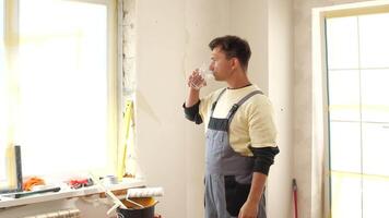 Construction worker taking a break, drinking water from a glass in an apartment undergoing renovation, with tools and materials visible on the windowsill video