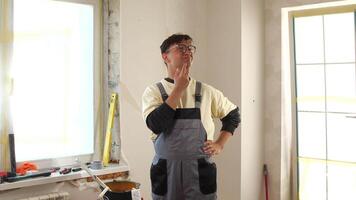 Painter in overalls stands thoughtfully in a renovated room, assessing the work done, with painting tools and materials scattered around, showcasing the process of home improvement video