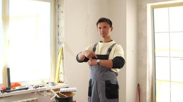 Construction worker pointing at his wristwatch, indicating it's time for a break during a home renovation project, surrounded by tools and materials video