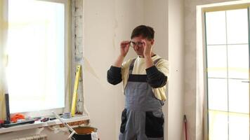 Exhausted builder rubbing his eyes while holding his glasses, taking a break during apartment renovation, demonstrating the physical demands of construction work video