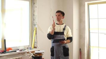 Construction worker wearing overalls takes notes on a clipboard while inspecting a home renovation project, demonstrating professionalism and attention to detail in the construction industry video