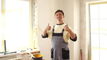 A man in overalls standing in a room with a thumbs up video