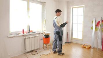 Contractor wearing overalls plans home renovation while taking notes on a clipboard in a room filled with tools and materials, focusing on design and project organization video