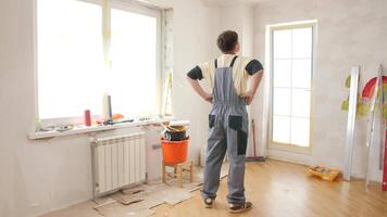 Painter standing with hands on hips, thoughtfully contemplating the artwork in a newly renovated room, surrounded by scattered painting tools and materials for the project video