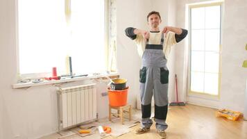 Painter wearing overalls showing thumbs down gesture, expressing disapproval and frustration with the renovation process in a room with painting tools and materials video