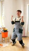 Vertical successful painter wearing overalls celebrating with raised fists in freshly painted room with bucket, broom, and paint tools visible, expressing joy and accomplishment video