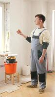 Vertical painter in overalls holding an apple, taking a break during apartment renovation, with paint buckets, rollers, and cleaning supplies visible in the background video